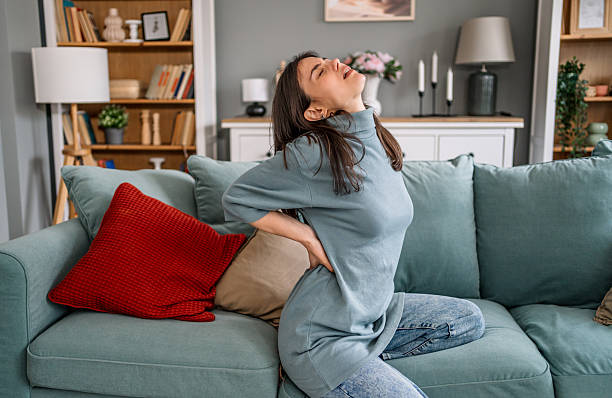 istock Woman suffering from back pain while sitting on sofa at home 2225089104