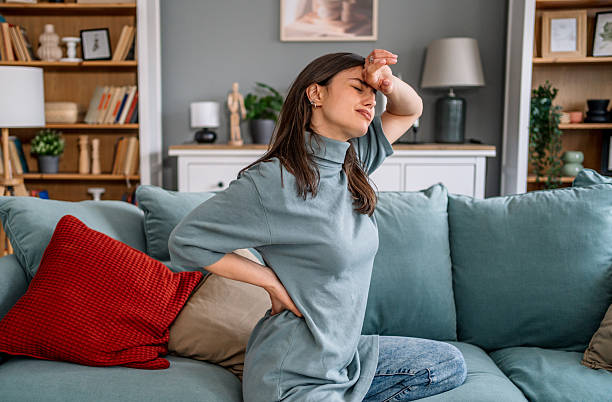 istock Young woman suffering from back pain while sitting on sofa 2225089125
