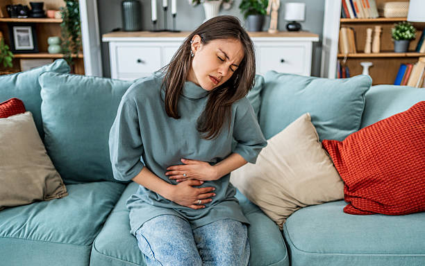istock Young woman suffering from strong stomach ache while sitting on sofa at home 2225089799