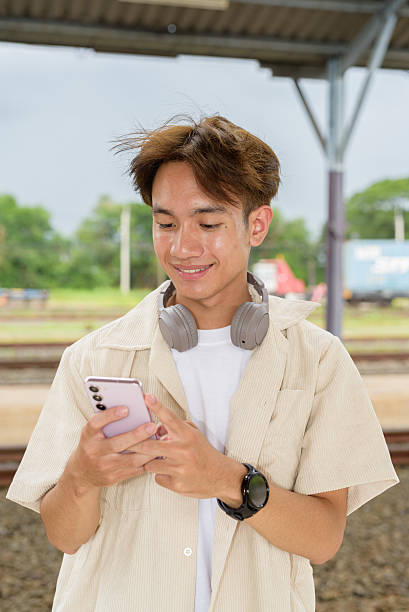 istock Young non binary tourist traveler in train station using phone 2225091170