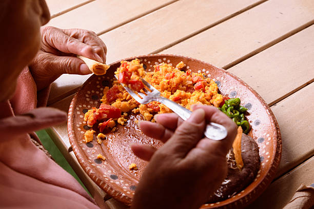 Unrecognizable elderly woman eating scrambled eggs for breakfast on a Mexican plate