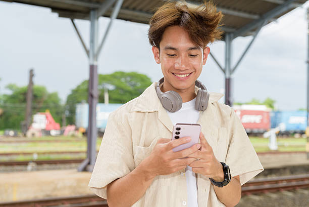 istock Young non binary tourist traveler in train station using phone 2225091726