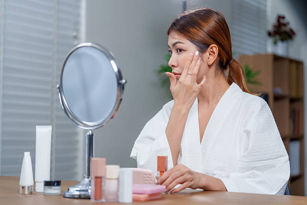 istock Woman in bathrobe applies makeup while looking in mirror, surrounded by various cosmetics. Her focus on beauty reflects serene moment of self care and confidence 2225093403