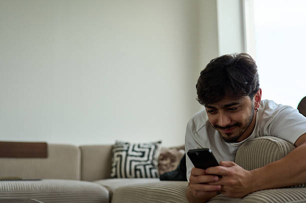 istock Young man relaxing on sofa using smartphone at home 2225099859