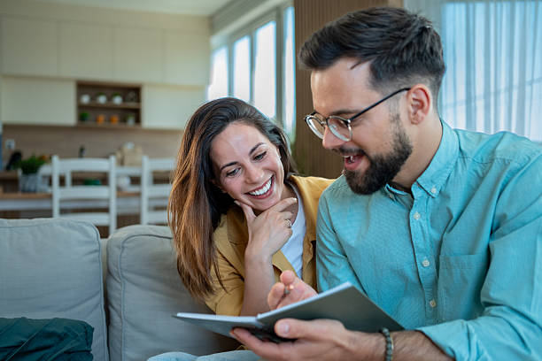 istock Happy couple reading notes and laughing together on sofa at home 2225101863