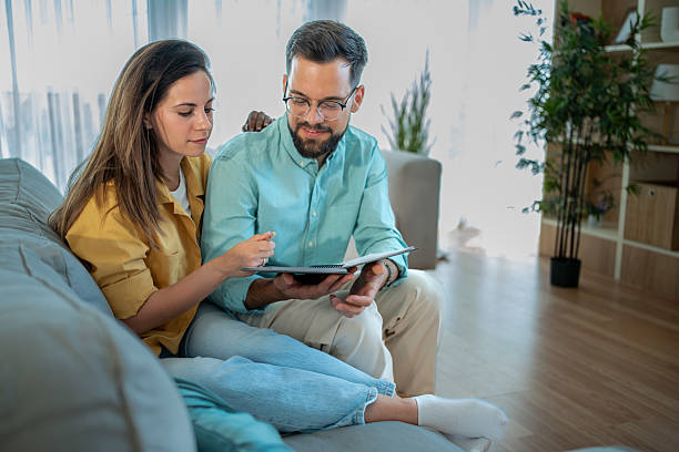 istock Young couple sitting on sofa and reading notes in notebook at home 2225102509