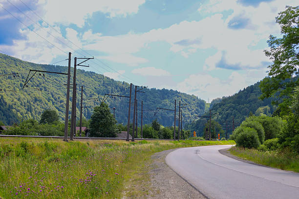 istock A curved asphalt road leads through mountainous terrain, surrounded by dense forests and tall power line poles. Under the summer sky, this landscape combines infrastructure with the natural beauty of the mountains. 2225104093
