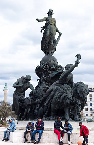 Paris, France - March 22, 2025: Boys and their fathers sit in front of the monument depicting Marianne, the symbol of France, at Place de la Nation. The monument is named “Triumph of the Republic.”