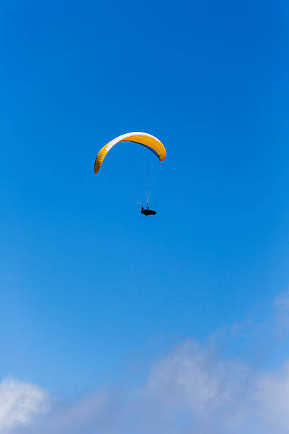 istock Bright yellow paraglider soaring through a clear blue sky over a serene landscape during a sunny afternoon 2225107631
