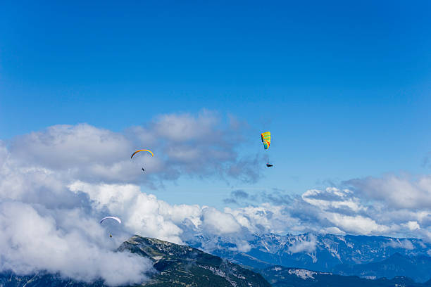 Paragliders glide gracefully through the air above majestic mountains, enjoying a sunny day with vibrant colors contrasting against the blue sky and fluffy clouds.