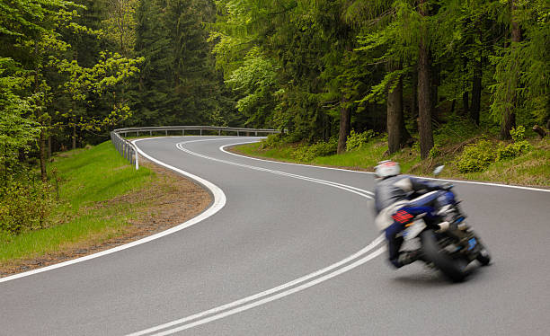 istock Motorcycle navigating a winding road through a lush forest landscape in springtime 2225108253