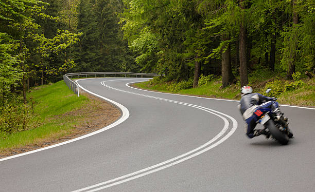istock Motorcyclist navigating a winding road through lush green forest in springtime 2225108270