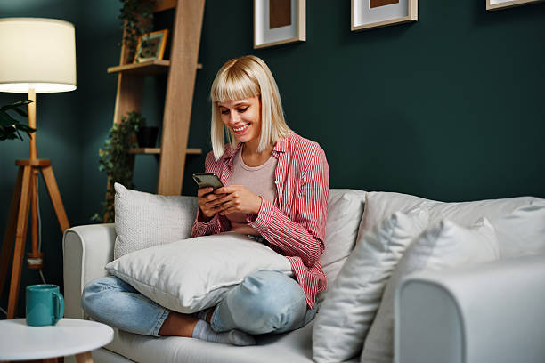 istock Smiling woman using smartphone on sofa at home 2225112258
