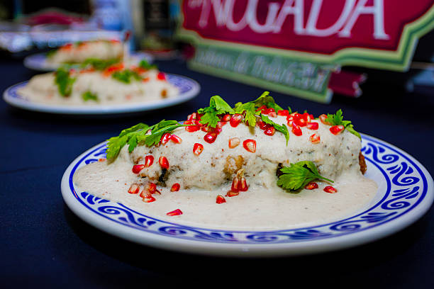 Seasonal Mexican dish made with poblano pepper stuffed with meat, covered in walnut sauce (nogada), and garnished with pomegranate and parsley. Served on a Talavera plate, celebrating Mexican heritage and independence season in August and September.