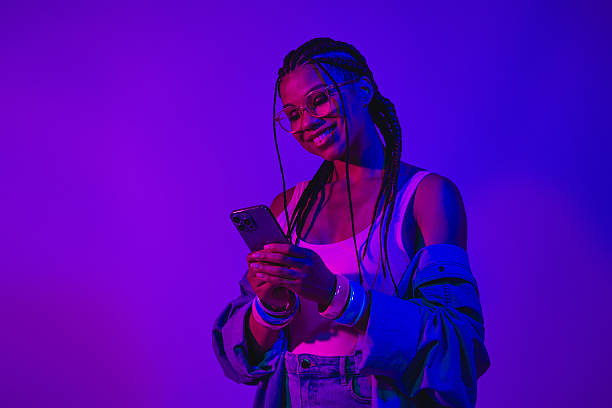 istock Young woman using mobile phone in neon lighting with a stylish denim outfit creating a modern vibrant atmosphere 2225117252