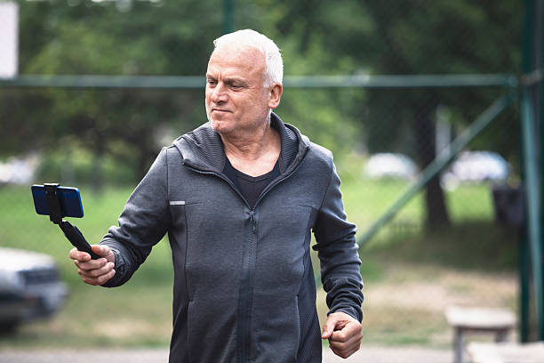 Sporty elderly man using phone and stabilizer to shoot fitness content outside.