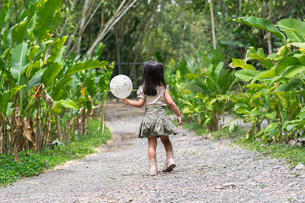 istock Latina toddler mid-step runs down pebbled zoo trail clutching white balloon surrounded by greenery. 2225118927