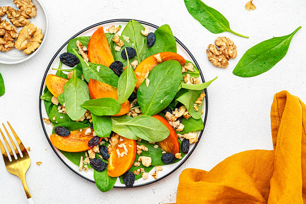 istock Autumn vegan salad with fresh persimmon, walnuts, raisin and spinach, white background, top view 2225122579