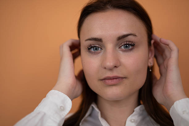 istock Young woman touching hair while looking at camera on orange background. Stock image 2225127961