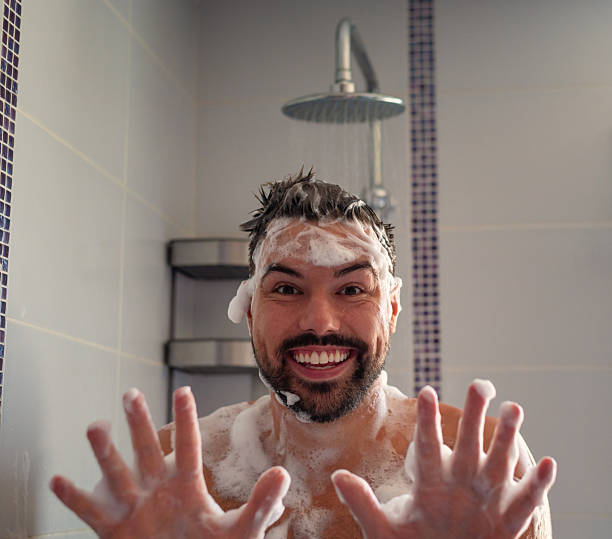 Young smiling man showering in the bathroom on a sunny morning.