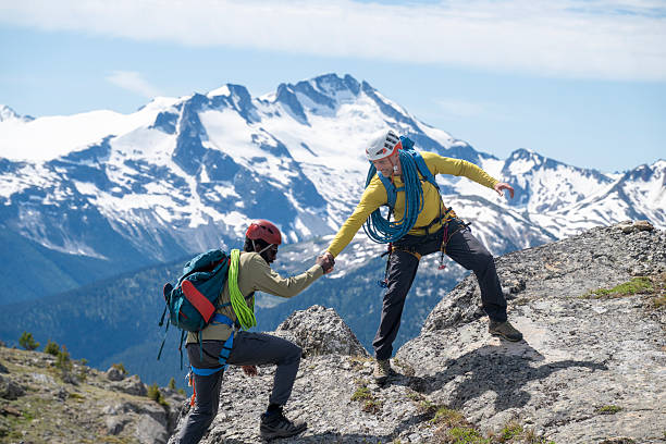 Climbing guide offers helping hand to  guest on mountain ridge, British Columbia Coastal Ranges