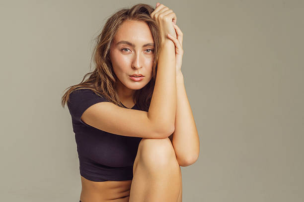 A young woman sits gracefully, showcasing her skin care routine, with soft lighting highlighting her features.