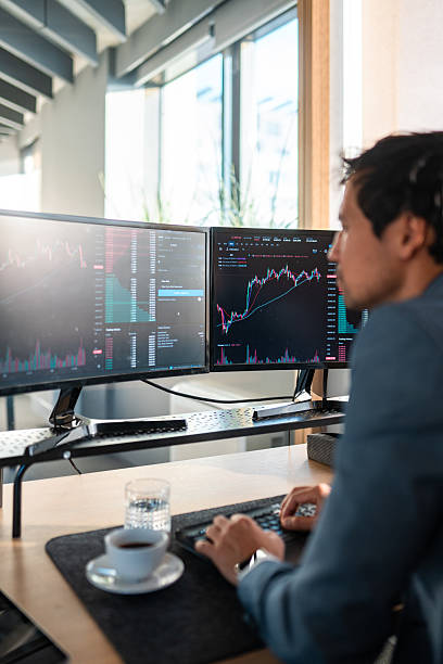 istock Focused Asian Stock Broker Analyzing Data on Dual Monitors 2225134542