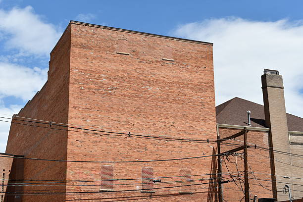 Looking up at corner of large brick building with no windows set against bright blue sky