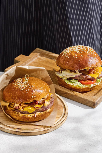 Gourmet burgers presented on wooden boards, bright lighting, closeup composition, chef’s hand partially visible