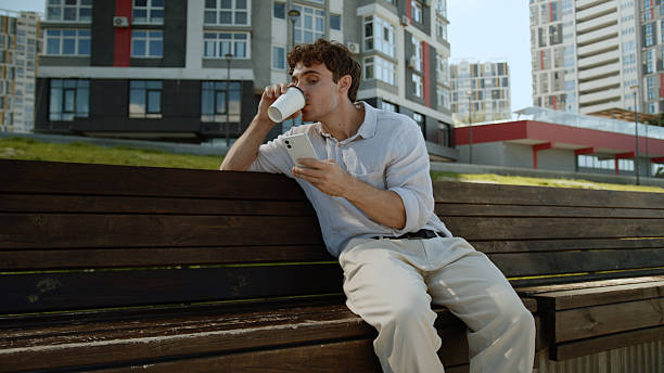 Caucasian man drinking coffee using mobile phone smartphone cellphone online employee entrepreneur internet social media funny smile businessman male business manager city worker guy enjoy outdoors. High quality 4k footage