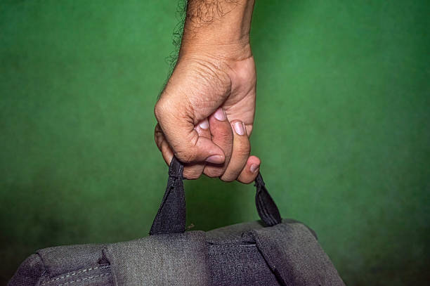 Hand gripping the black strap of a rugged backpack against a green backdrop, showcasing strength, texture, and functionality. Ideal for outdoor, travel, or lifestyle visuals