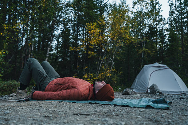 Person performing relaxation exercises on a mat in a serene forest campsite surrounded by nature.
