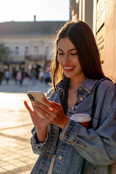 istock Young woman using smartphone and holding coffee in city square 2225152765