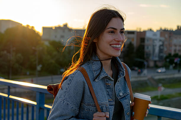 istock Young woman walking on a bridge at sunset, drinking coffee 2225152922