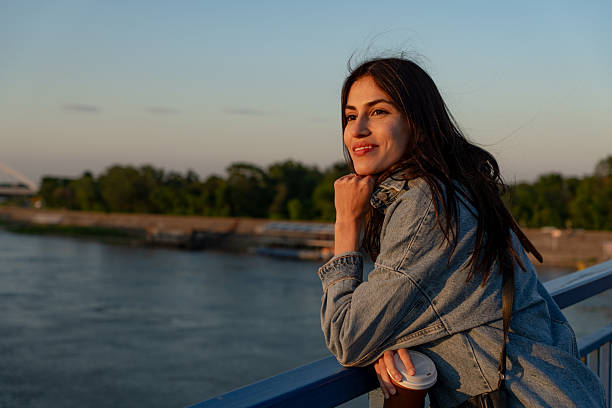 istock Young woman enjoying sunset view from bridge with takeaway coffee 2225153029
