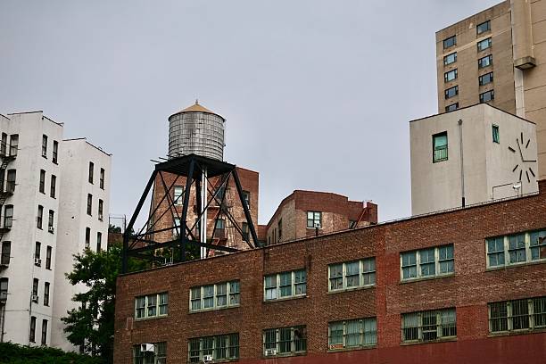 A traditional wooden rooftop water tower perched on top of a brick building in Manhattan, New York City. The image highlights an iconic element of the city’s architectural identity, set against a vivid blue sky. These water towers, still in use today, are a defining feature of the urban landscape and a symbol of New York’s historic infrastructure.