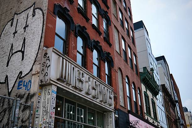New York, New York, USA – July 11, 2025:  Old and new buildings crowd together in SoHo, with graffiti-tagged walls and vintage wine signage on the Bowery.