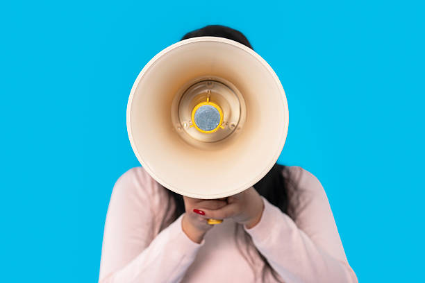 istock Person holding a megaphone in front of a bright blue background while promoting a cause or event 2225164729