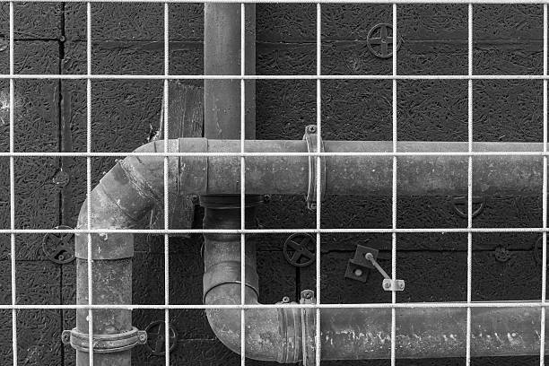 A network of industrial pipes intersects with a metal grid, showcasing urban infrastructure. The setting highlights the contrast between metal surfaces and the surrounding walls.