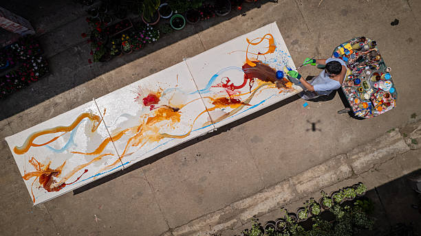 One man, painting in his open-air studio, with his canvas in front of him, viewed from above. Painter. Open-air studio. Abstract. Expressive. Man. Canvas. Paint.