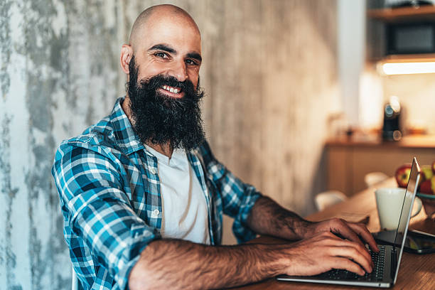 istock Smiling man sitting at a wooden table working on a laptop 2225169414