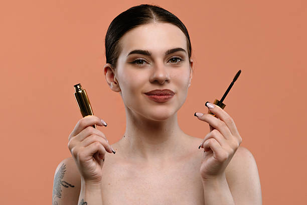Woman Holding Mascara with Confident Expression on Orange Background