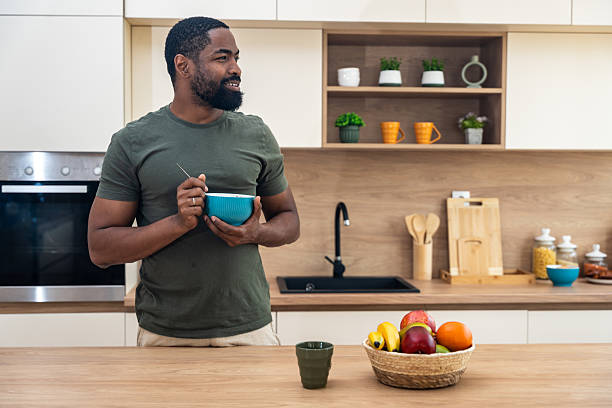 istock Morning routine, simple living. One man standing in the kitchen, drinking coffee, eating healthy breakfast. Male entrepreneur at home, starting his day casual and relaxed. 2225172445
