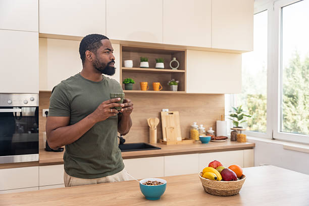 istock Morning routine, simple living. One man standing in the kitchen, drinking coffee, eating healthy breakfast. Male entrepreneur at home, starting his day casual and relaxed. 2225172447