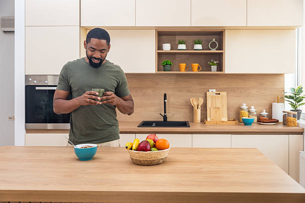 istock Morning routine, simple living. One man standing in the kitchen, drinking coffee, eating healthy breakfast. Male entrepreneur at home, starting his day casual and relaxed. 2225172461