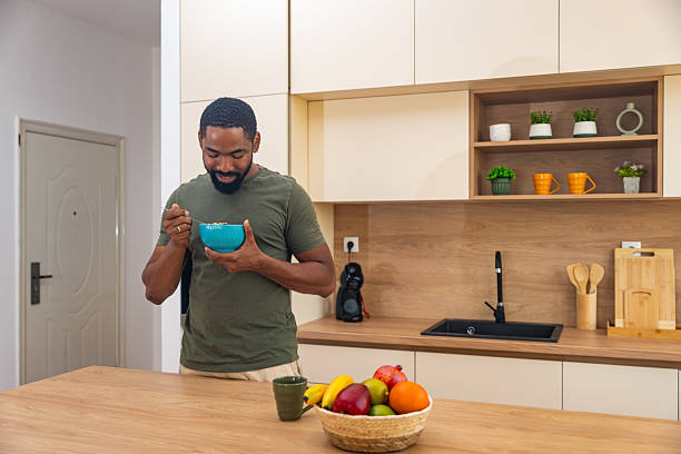 istock Morning routine, simple living. One man standing in the kitchen, drinking coffee, eating healthy breakfast. Male entrepreneur at home, starting his day casual and relaxed. 2225172474