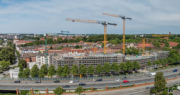 istock Panoramic view of large urban construction site with four cranes, scaffolding-covered buildings, residential homes in the background and road with traffic in front. Construction site in Kiel, Germany. 2225176186