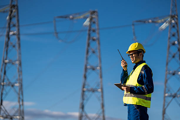 istock Technician communicates via radio in high-visibility vest near electrical pylons, under blue sky. 2225178522