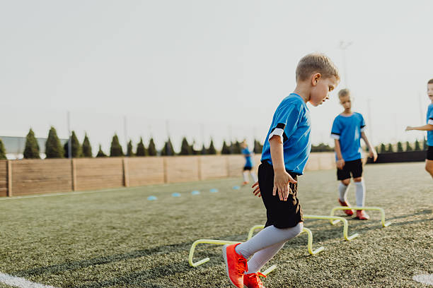A wide shot of a group of children wearing sports clothing, football boots and sports bibs on a football pitch in the North East of England. They are at football practice where they are doing training drills.