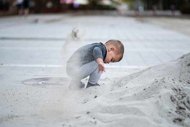 Baby dropping sand in an urban playground, enjoying the textures while developing fine motor skills and embracing joyful exploration